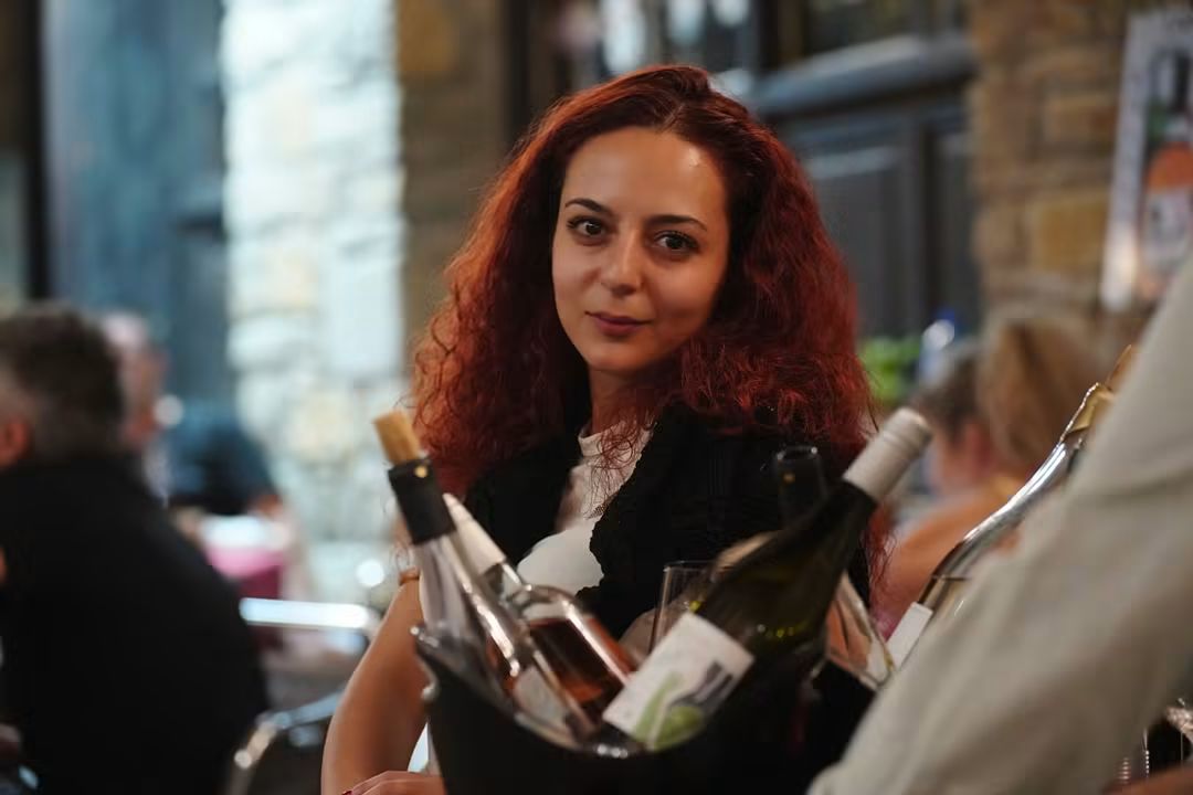 Домакиня зад охладител с бутилки, в топлата светлина на залата.